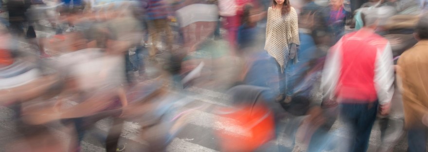 A woman stands among a crowd of blurry people.